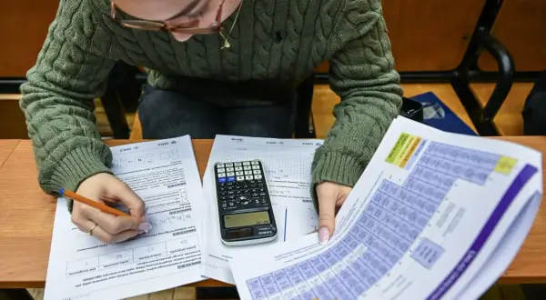 Uczeń pisze egzamin, przed nim leżą arkusze z zadaniami, kalkulator i układ okresowy pierwiastków.
