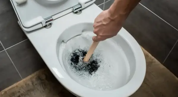 Hand plunges a toilet that is verstopft immer wieder. Water splashes around the plunger.