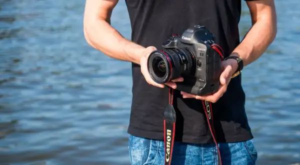 Mężczyzna trzyma aparat Canon EOS-1D Mark II z obiektywem, idealny do fotografii krajobrazowej dzięki matrycy APS-C.
