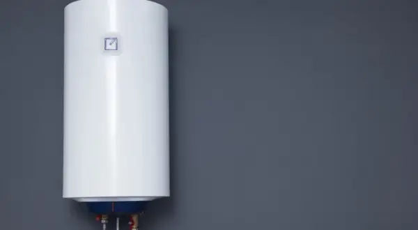 Biały bojler elektryczny wiszący na szarej ścianie.