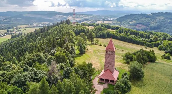 Kamienna wieża widokowa na wzgórzu, otoczona lasami i polami. Jedna z wielu wież widokowych na Dolnym Śląsku, oferująca piękne krajobrazy.