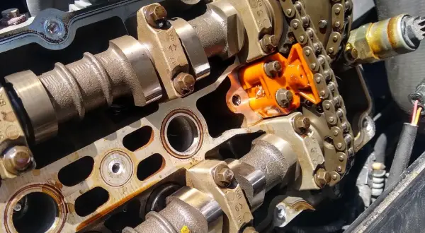 Detalle de un motor con el árbol de levas y el cigüeñal expuestos, junto a una cadena de distribución naranja.