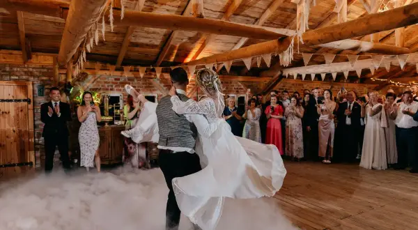 Para młoda tańczy na weselu w dymie. Goście obserwują ich taniec, zastanawiając się, ile trwa wesele.
