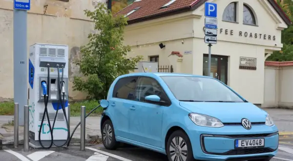 Niebieski Volkswagen Up ładuje się przy stacji ładowania. Obok znajduje się budynek z napisem "COFFEE ROASTERS".