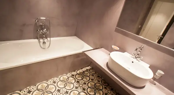 Baño moderno con microcemento en paredes y suelo de baldosas hidráulicas. Bañera y lavabo de diseño.