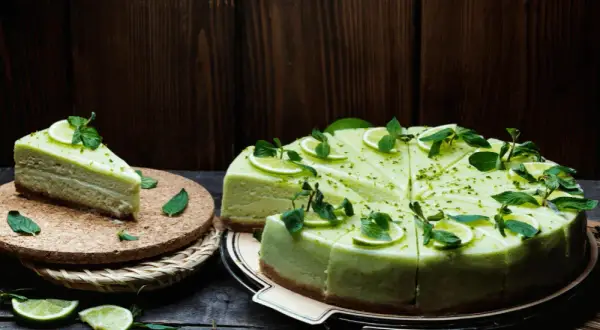 Zielony, orzeźwiający sernik pistacjowy, udekorowany plasterkami limonki i listkami mięty, kusi swoim wyglądem.