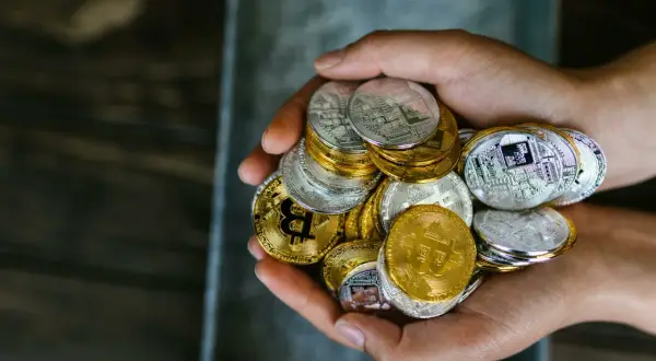Mani che stringono una manciata di monete d'oro e d'argento, simboleggiando i criptovalute rischi e vantaggi.