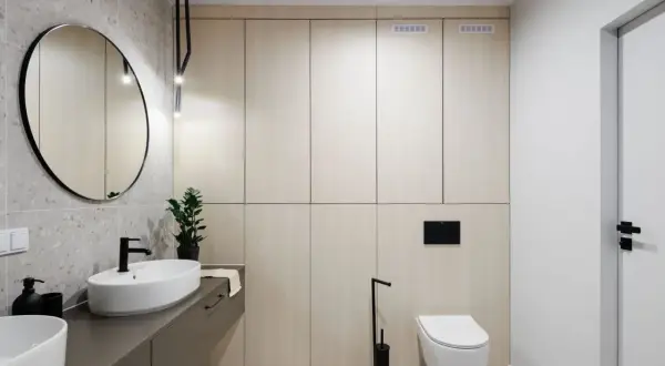 Nowoczesna łazienka z zabudową WC z płyty meblowej, umywalką nablatową i okrągłym lustrem.