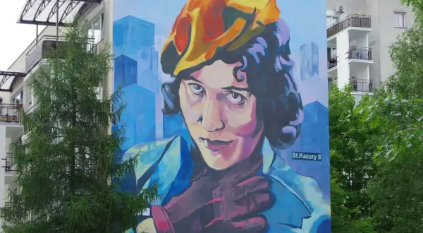 Mural przedstawiający Zofię Stryjeńską w żółtym beretce, z dłonią na piersi. Tło to błękitne, geometryczne budynki.