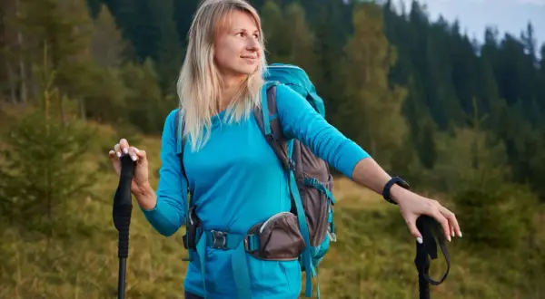 Frau mit Rucksack und Wanderstöcken in den Bergen. Wandern ist eine tolle Aktivität für den Kalorienverbrauch.