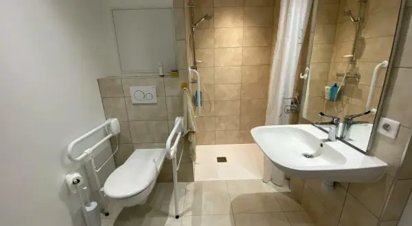 Salle de douche pmr avec WC adapté, barre d'appui, lavabo et douche à l'italienne. Confort et sécurité assurés.