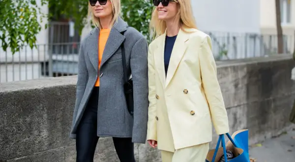 Dwie kobiety w stylowych marynarkach. Jedna w szarej, oversize, druga w pastelowej, żółtej. Obie w okularach przeciwsłonecznych.