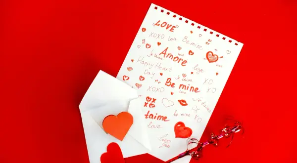 Une feuille blanche ornée de mots d'amour et de cœurs rouges, sortant d'une enveloppe. Un texte touchant pour son parrain.