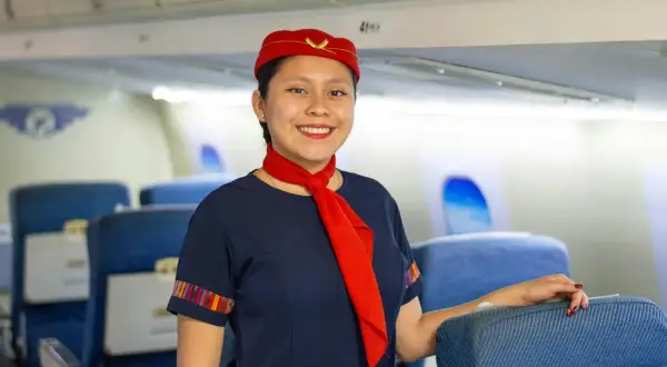 Uśmiechnięta stewardessa w granatowym mundurku i czerwonym beretku, gotowa do lotu. Marzysz, jak zostać stewardessą?