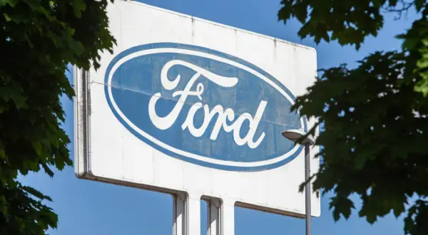 Großes Ford-Logo auf einem Schild, umgeben von grünen Blättern. Vielleicht ein Zeichen für eine neue Ära oder eine ford abfindung.