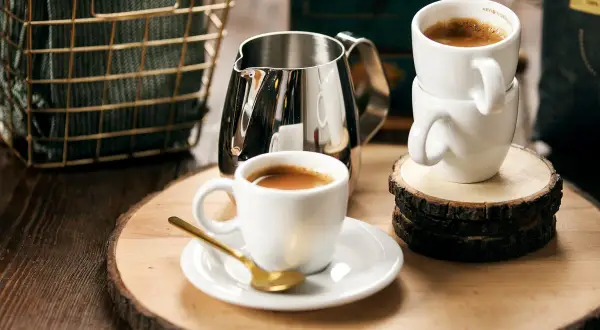 Enkel espresso med gyllene sked och mjölkkanna. Två koppar står staplade på träbitar.