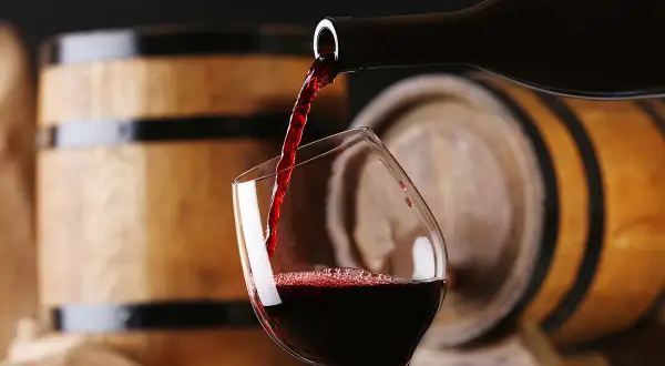 Versando un ricco aglianico vino in un bicchiere, con botti di legno sullo sfondo.