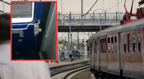 Zbliżenie na mechanizm drzwi pociągu, pokazujący, jak otworzyć drzwi w pociągu, z widokiem na peron i tory.