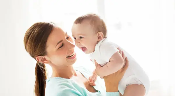 Szczęśliwa mama trzyma roześmiane dziecko. Zastanawiasz się, ile pieluch dziennie dla noworodka?