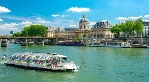 Bateau touristique sur la Seine, avec l'Institut de France et un pont en arrière-plan. Une belle journée pour une visite Paris Seine.