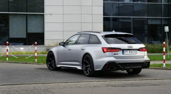 Srebrne Audi RS6 Avant z czarnymi felgami stoi na parkingu przed nowoczesnym budynkiem.