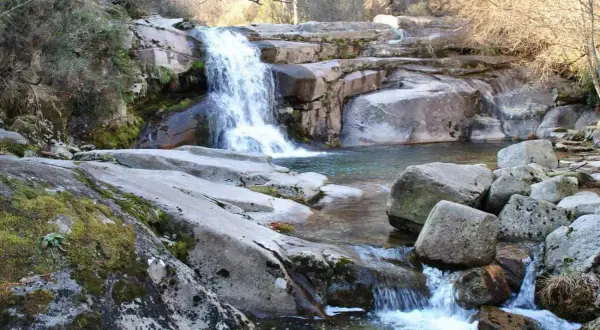Cascada y charcas naturales en Ourense, rodeadas de rocas cubiertas de musgo y vegetación.
