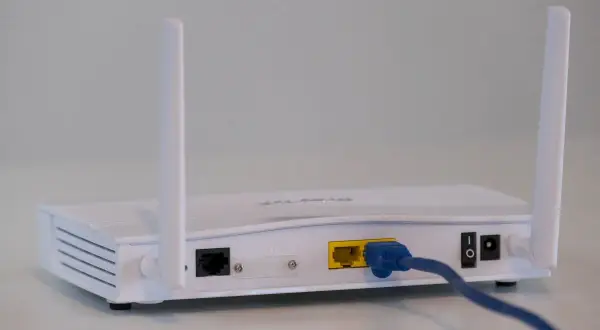 Biały router z dwiema antenkami, portem LAN i kablem sieciowym. To urządzenie, które pozwala połączyć się z internetem, czyli co to jest modem.