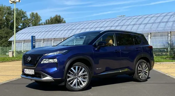 Niebieski Nissan X-Trail na tle hali sportowej. Wiele osób szuka nissan x trail opinie, ten SUV może być dobrym wyborem.