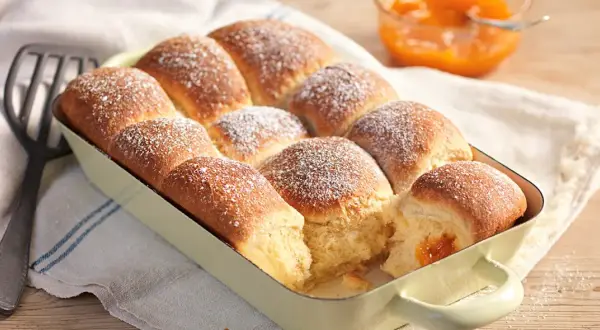 Frisch gebackene Buchteln, bestäubt mit Puderzucker, warten darauf, mit Marillenmarmelade gefüllt zu werden. Ein echtes Buchteln original Rezept.