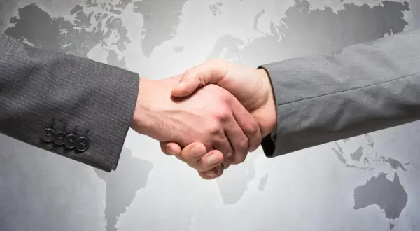 Uścisk dłoni dwóch mężczyzn w garniturach na tle mapy świata. Symbolizuje globalne partnerstwo i ddp.