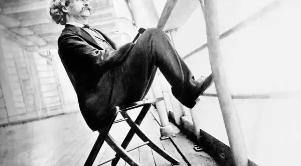 Mark Twain sitter på en stol på ett skeppsdäck, med en hatt och en mustasch. En bild som inspirerar till ett mark twain citat om livet.
