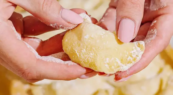 Dłonie z pudrowym cukrem delikatnie formują pyszne pierogi z serem.