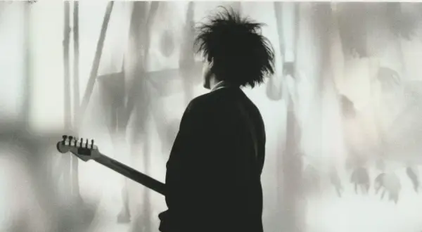 Chłopcy nie płaczą. Robert Smith z The Cure z gitarą, w cieniu, z charakterystyczną fryzurą.