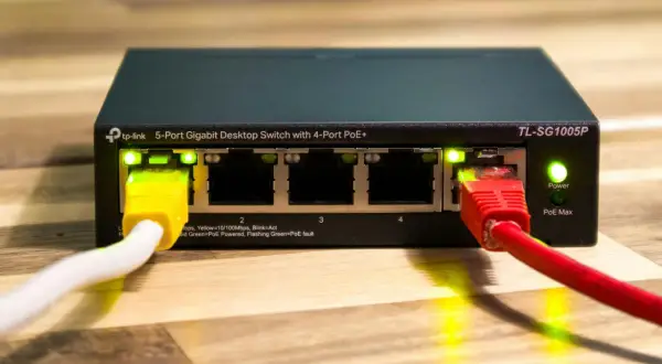Zarządzalny switch TP-Link TL-SG1005P z 5 portami Gigabit Ethernet i 4 portami PoE+. Podłączone kable sieciowe, świecące diody LED.
