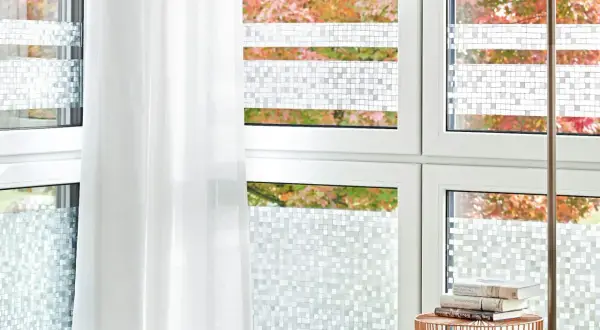 Fenster mit statischer Fensterfolie im Mosaikmuster, die Privatsphäre schafft. Ein weißer Vorhang hängt daneben.