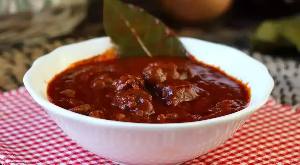 En mustig sås till korv, med köttbitar och lagerblad i en djup röd sås. Perfekt för en mysig middag.