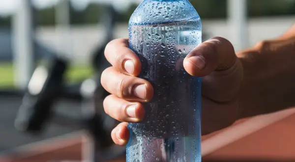 Main d'un sportif tenant une bouteille d'eau fraîche, idéale pour boire de l'eau avec du sel après l'effort.