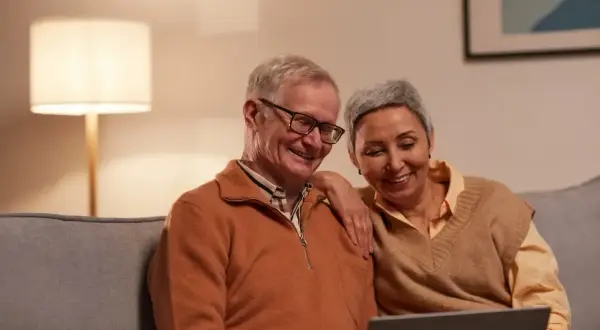 Uśmiechnięta para seniorów przegląda coś na laptopie. Może planują urlop bezpłatny, by cieszyć się emeryturą.