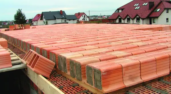 Strop ackermana w budowie, rzędy pustaków ceramicznych czekają na betonowanie. W tle domy z czerwonymi dachami.