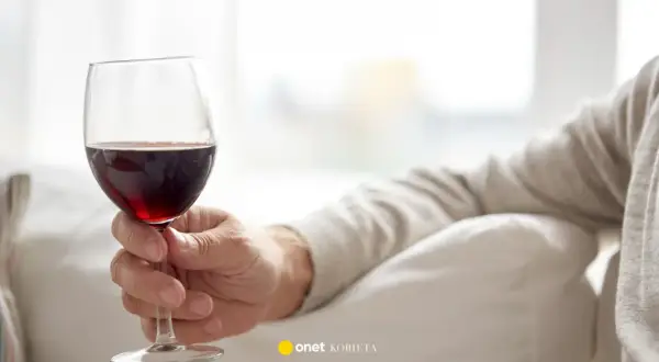 Dłoń trzyma kieliszek czerwonego wina. Czy czerwone wino obniża ciśnienie? Warto to sprawdzić.