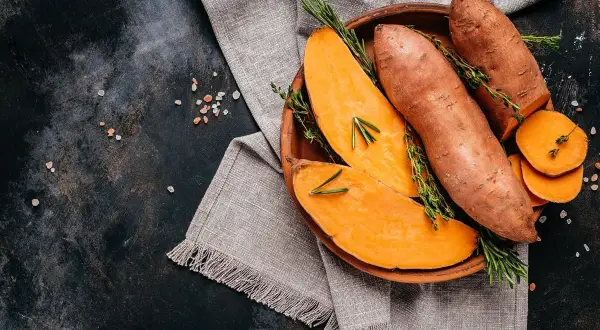 Pomarańczowy batat, pokrojony i w całości, z gałązkami rozmarynu i tymianku, na glinianej misce.