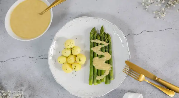 Spargel mit kleinen Kartoffeln und einer cremigen, veganen Sauce Hollandaise. Ein goldener Löffel liegt bereit.