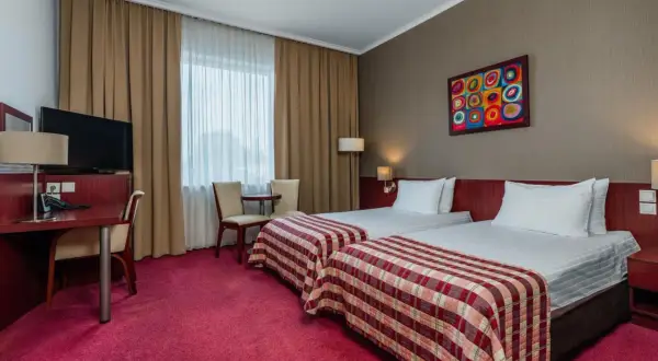 Pokój w hotelu Premier Kraków z dwoma wygodnymi łóżkami, biurkiem i kolorowym obrazem na ścianie.