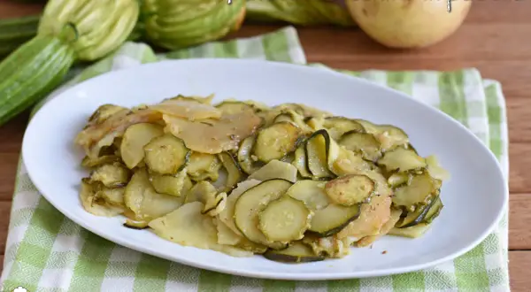 Piatto di zucchine e patate cotte in padella, con zucchine fresche e patate affettate, su un tovagliolo a quadretti verdi.