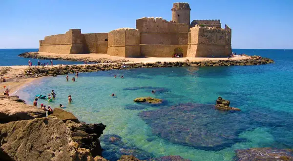 Castello Aragonese su un'isola con mare cristallino, bagnanti e rocce. Un vero spettacolo del **calabria mare bello**.