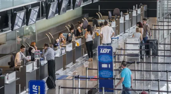 Kolejka do odprawy na lotnisku. Ludzie czekają na boarding, pracownicy obsługują stanowiska.