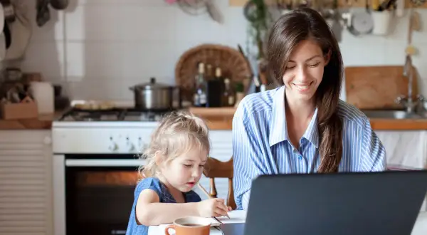 Frau arbeitet am Laptop, Kind malt daneben. Ein Beispiel für Home Office Sicherheit, wo Familie und Beruf harmonisch vereint werden.