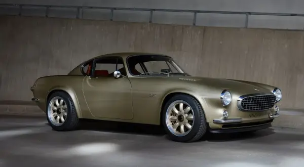 En gyllene Volvo P1800, en tidlös klassiker med en modern touch, står parkerad mot en betongvägg.