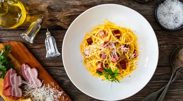 En tallrik krämig spaghetti carbonara med pancetta, toppad med parmesan och persilja. Perfekt vin till carbonara.