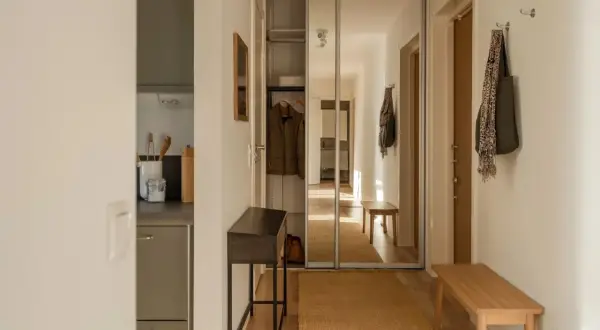 En hall med en träbänk, en smal konsol och en stor spegelgarderob. Hållbar inredning med naturliga material som jute och trä.